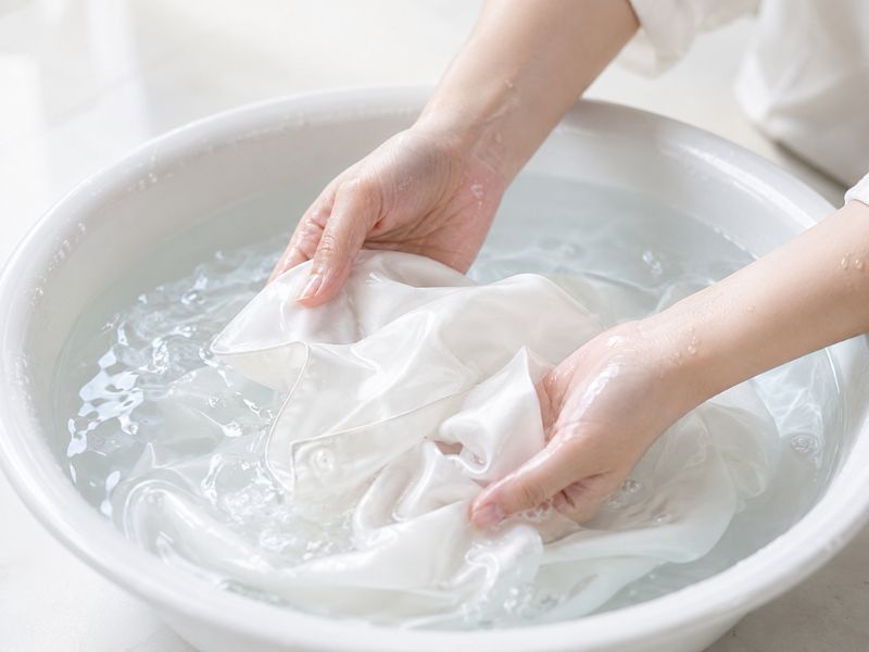 Frau wäscht eine weiße Seidenbluse sanft mit der Hand im kalten Wasser